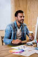 Graphic designer working on his graphics tablet and holding coff