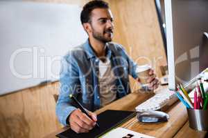 Man working on his graphics tablet and holding coffee