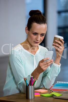 Woman holding coffee cup and text messaging on mobile phone