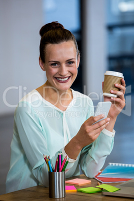 Woman holding coffee cup and text messaging on mobile phone