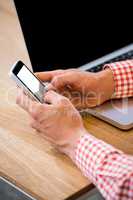 Man text messaging on mobile phone with laptop on desk