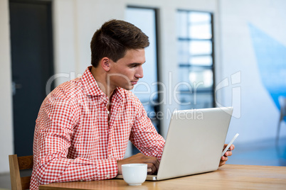 Man text messaging on mobile phone while using laptop