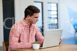 Man text messaging on mobile phone while using laptop