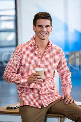 Portrait of happy man sitting on desk with coffee