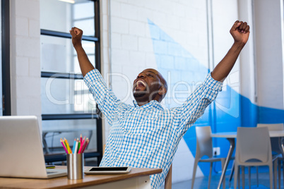 Excited man sitting on table with digital tablet and laptop