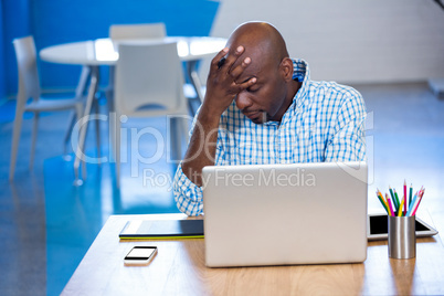 Tense man sitting on table with laptop and graphics tablet
