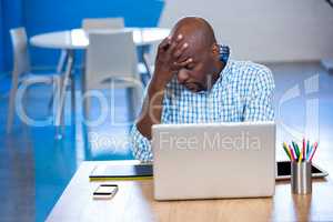 Tense man sitting on table with laptop and graphics tablet