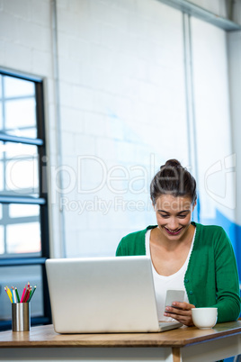Woman using mobile phone with laptop on table