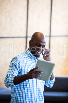 Man looking at digital tablet while talking on phone Man looking at digital tablet while talking on phone