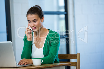 Woman talking on phone while using laptop