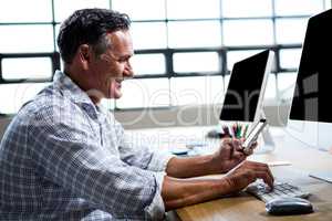 Man text messaging on mobile phone while using computer