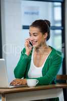 Woman talking on phone while using laptop