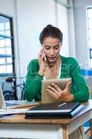 Woman looking at digital tablet while talking on phone