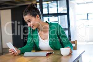 Woman text messaging on mobile phone while having cup of coffee