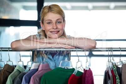 Portrait of a happy woman leaning on clothes display stand