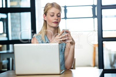 Woman using mobile phone with laptop on table