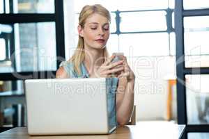 Woman using mobile phone with laptop on table