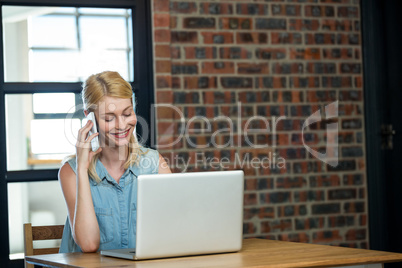 Woman talking on phone while using laptop