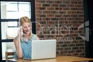 Woman talking on phone while using laptop