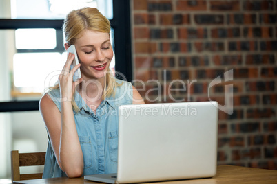 Woman talking on phone while using laptop Woman talking on phone while using laptop