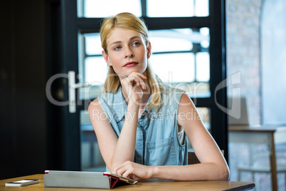 Thoughtful woman sitting on table with keyboard and mobile phone