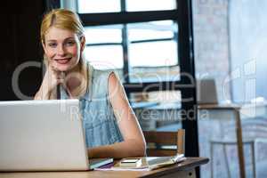 Portrait of happy woman sitting at desk with laptop and mobile p
