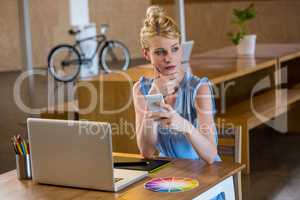 Graphic designer in office sitting at desk and holding mobile ph