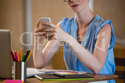 Graphic designer in office sitting at desk and text messaging on