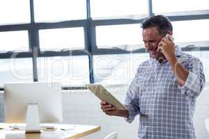 Man looking at digital tablet while talking on phone