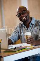 Graphic designer using laptop in office and holding a coffee