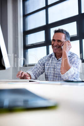 Man talking on mobile phone while using computer