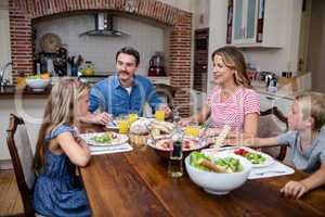 Happy family talking to each other while having meal in kitchen