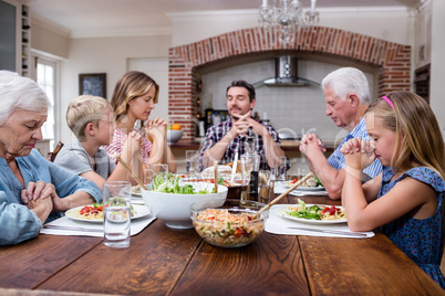 Multi-generation family praying before having meal