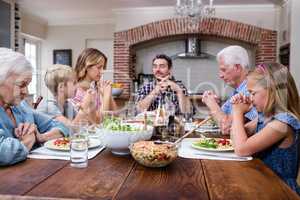 Multi-generation family praying before having meal