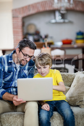 Father and son using laptop in living room