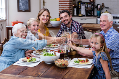 Multi-generation family toasting glass of wine while having meal