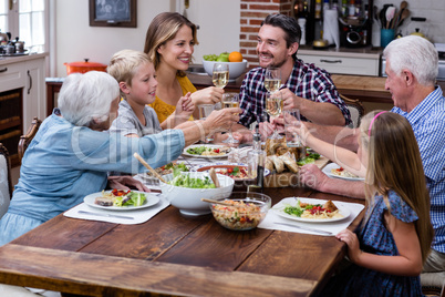 Multi-generation family toasting glass of wine while having meal