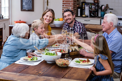Multi-generation family toasting glass of wine while having meal