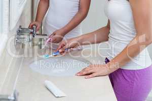 Mid section of mother and daughter washing their toothbrush in w