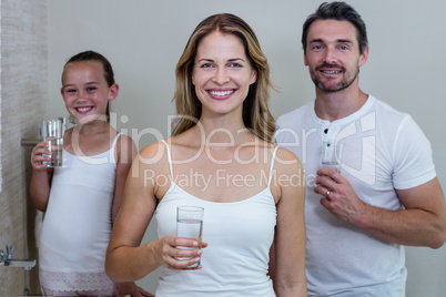 Parents and daughter holding a glass of water in bathroom