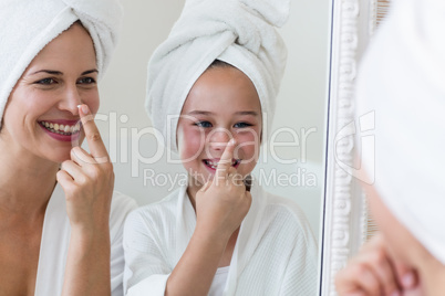 Smiling mother and daughter applying moisturizer on nose