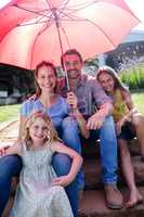 Happy family sitting in garden under a red umbrella