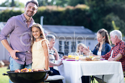 Father and daughter at barbecue grill while family having lunch