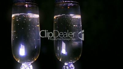 Bubbling champagne being poured into two crystal glasses against black