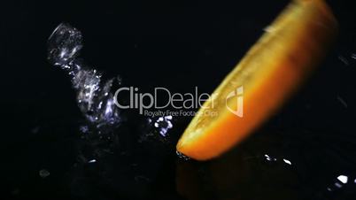 Slow motion of lemons falling with water drops on black surface.