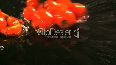 Slow motion of tomatoes falling with water drops on black surface.