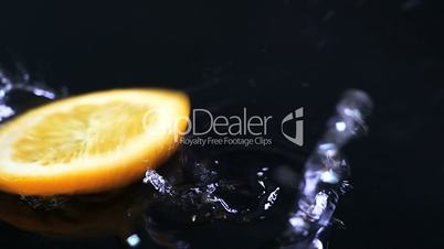 Slow motion of lemons falling with water drops on black surface.