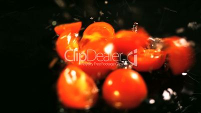 Slow motion of tomatoes falling with water drops on black surface.