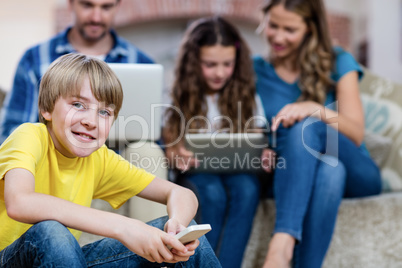Portrait of boy using a mobile phone while family in background