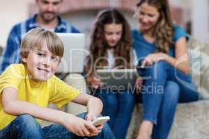 Portrait of boy using a mobile phone while family in background